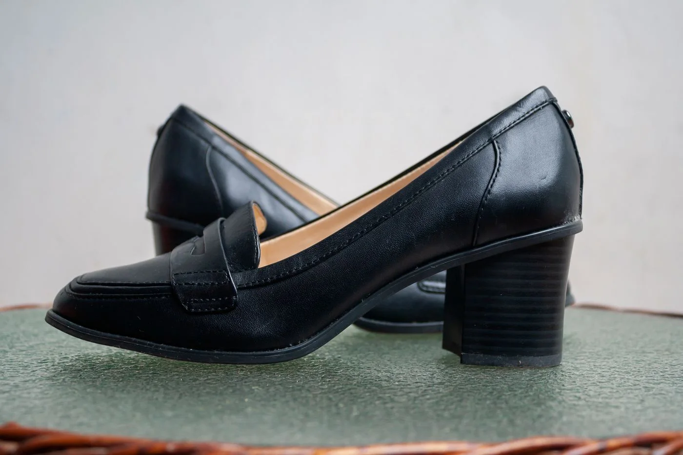Pair of dark slip-on shoes with low block heels on a green surface.