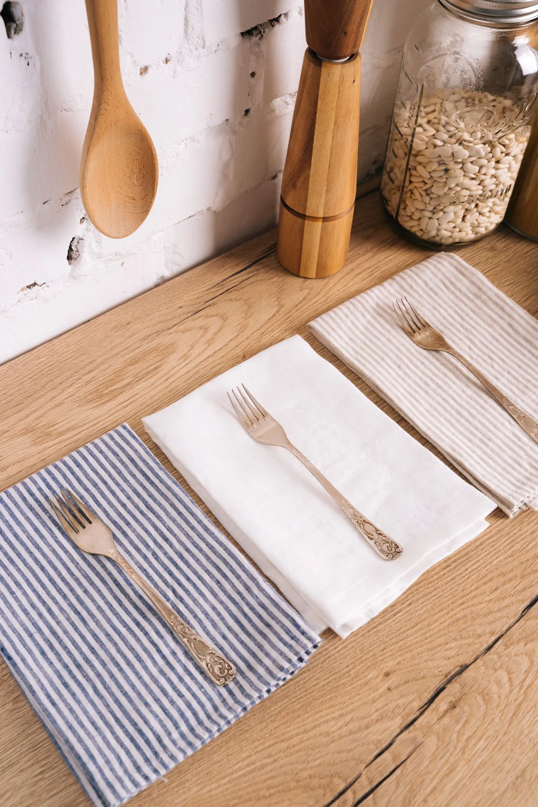 Two striped kitchen towels and cutlery on a wooden worktop.