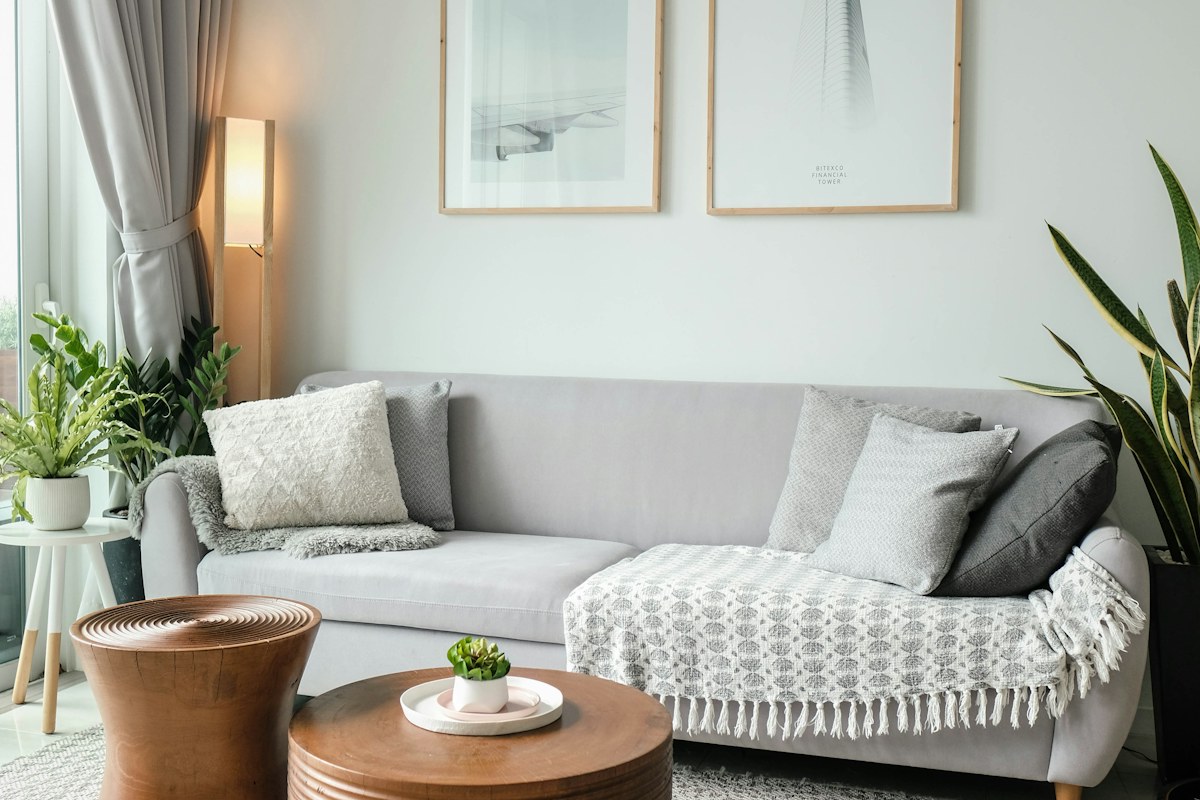Gray sofa, cushions, plants and wooden tables in a bright living room.