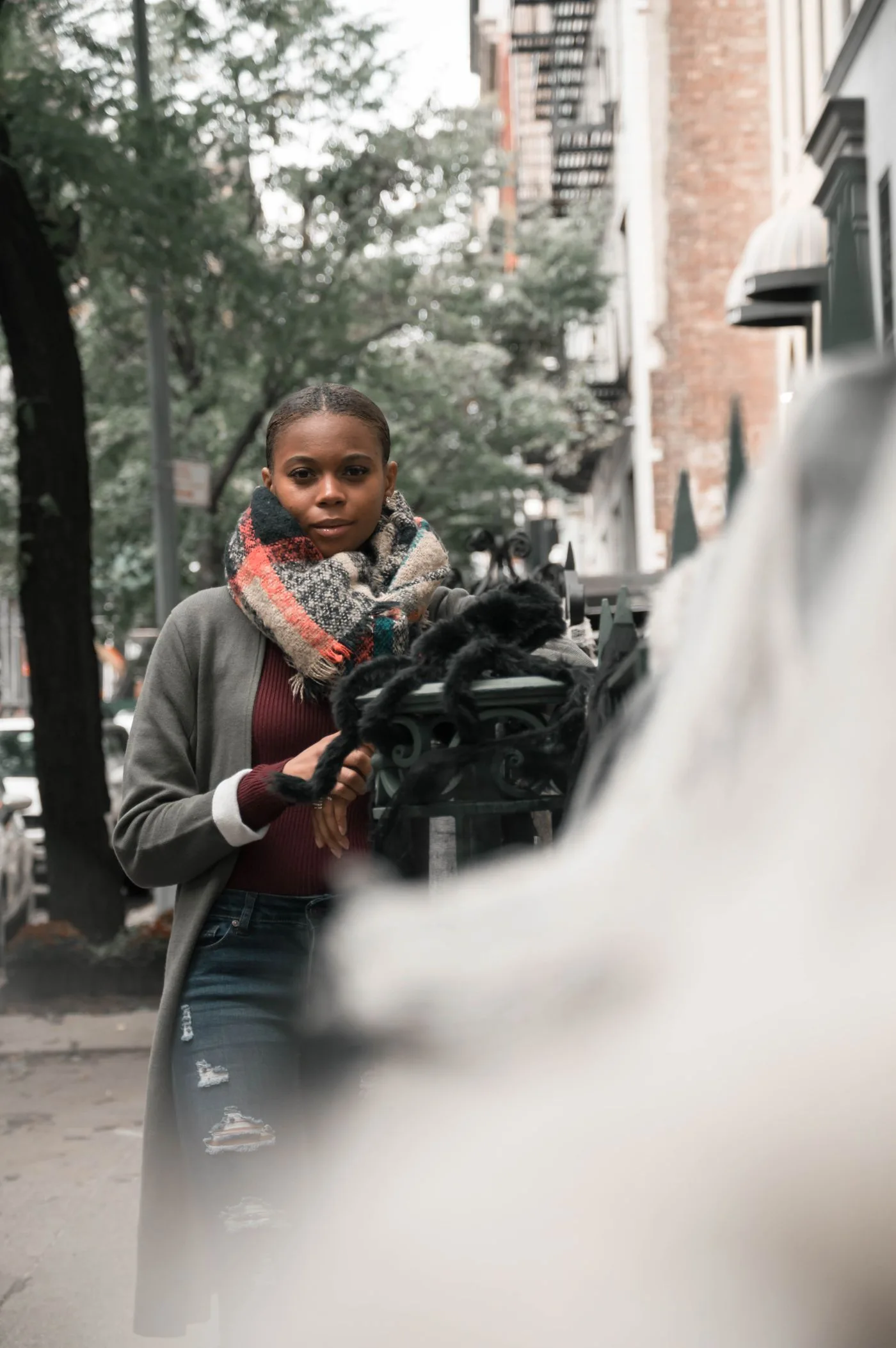 Woman wearing a gray coat and patterned scarf on a street.