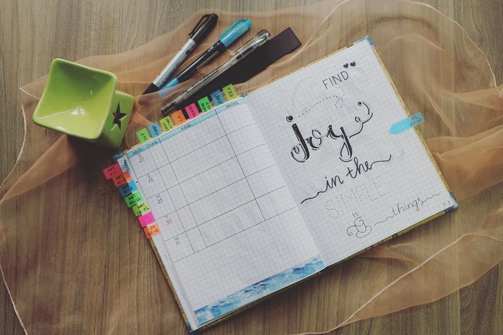 Open planner, pens and stationery on a wooden table.