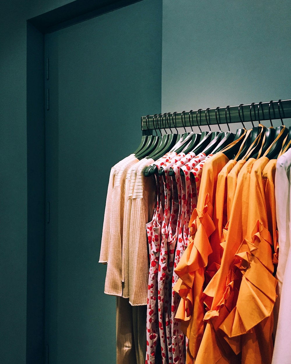Light and brightly coloured garments hanging on a rail against a dark green wall.