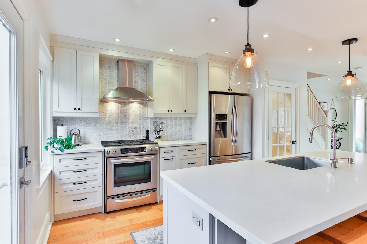 White kitchen cabinets and a pale island beneath hanging lights