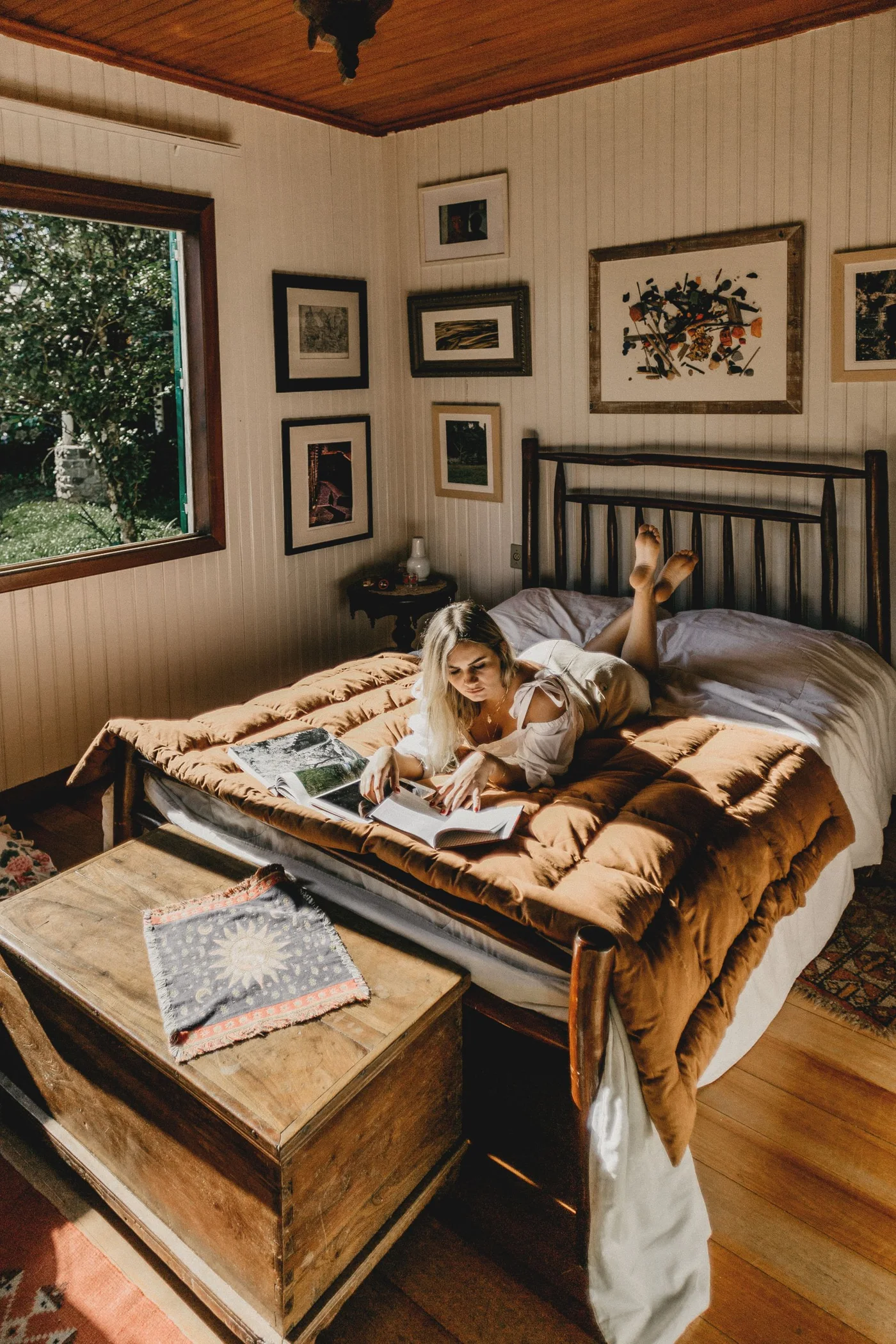 Woman reading on a bed beneath a gallery of framed pictures