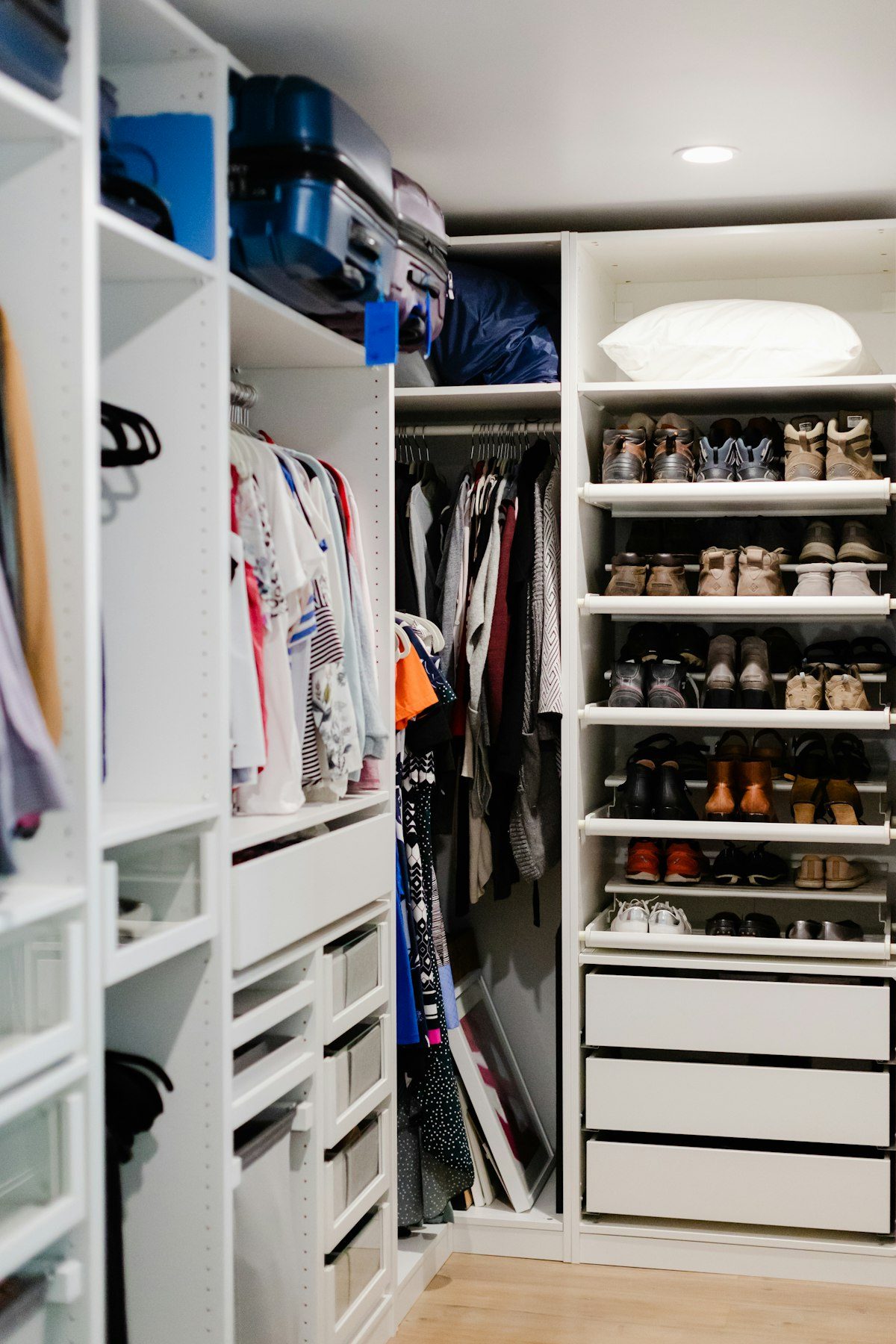 White walk-in wardrobe containing hanging clothes, folded items and shoes