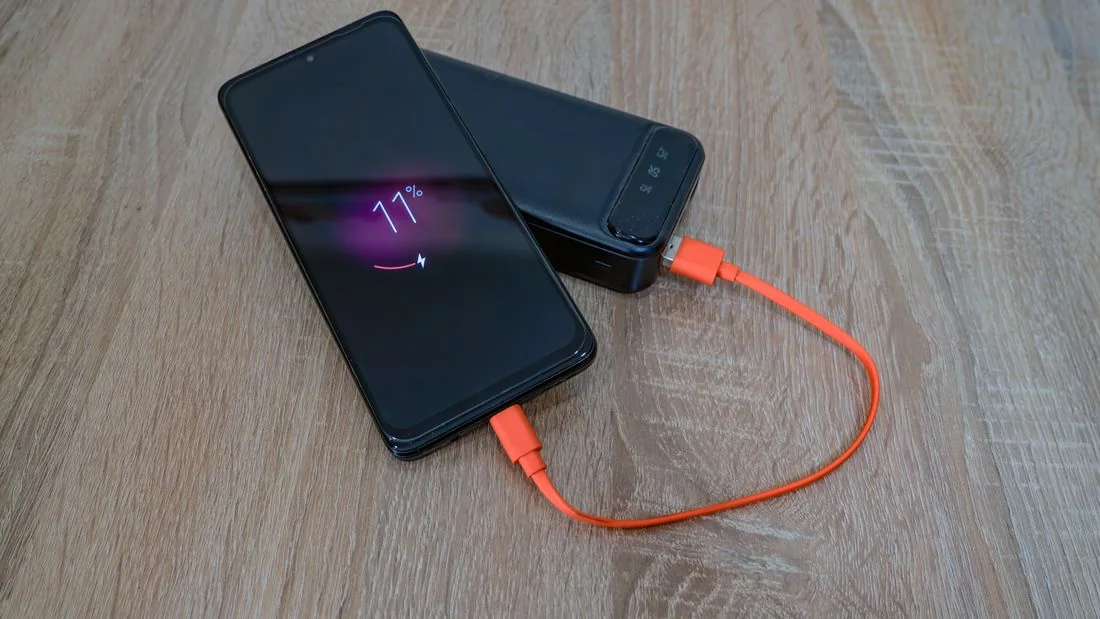 Smartphone and portable battery connected by a bright orange cable on a wooden surface