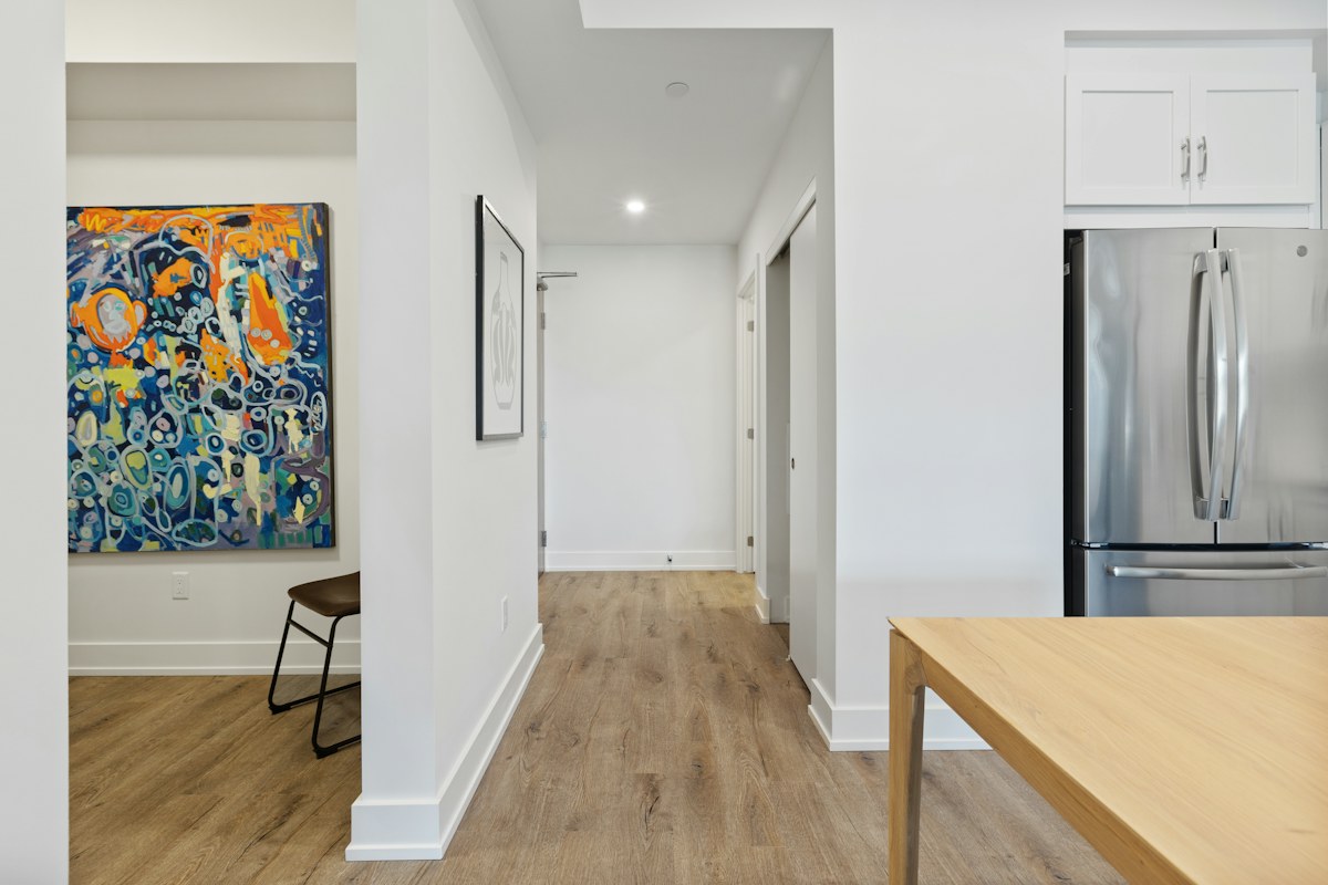 A bright hallway opening into a kitchen with a wooden worktop and a framed colourful painting.