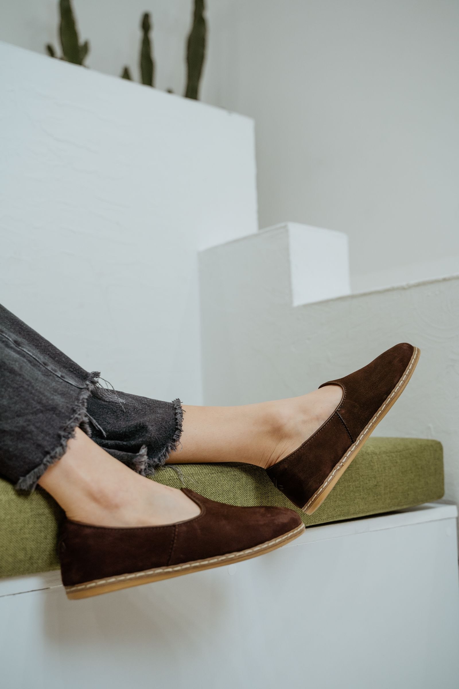 Brown loafers worn with frayed blue jeans beside a pale staircase.