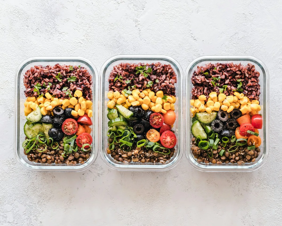 Three matching food containers filled with vegetables and grains on a pale surface.