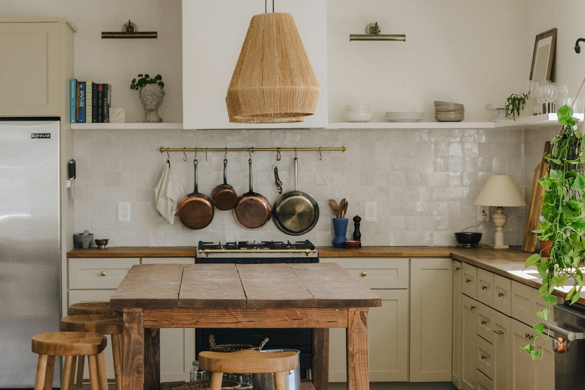 A rustic kitchen with a wooden island, stools and pans hanging along the wall.
