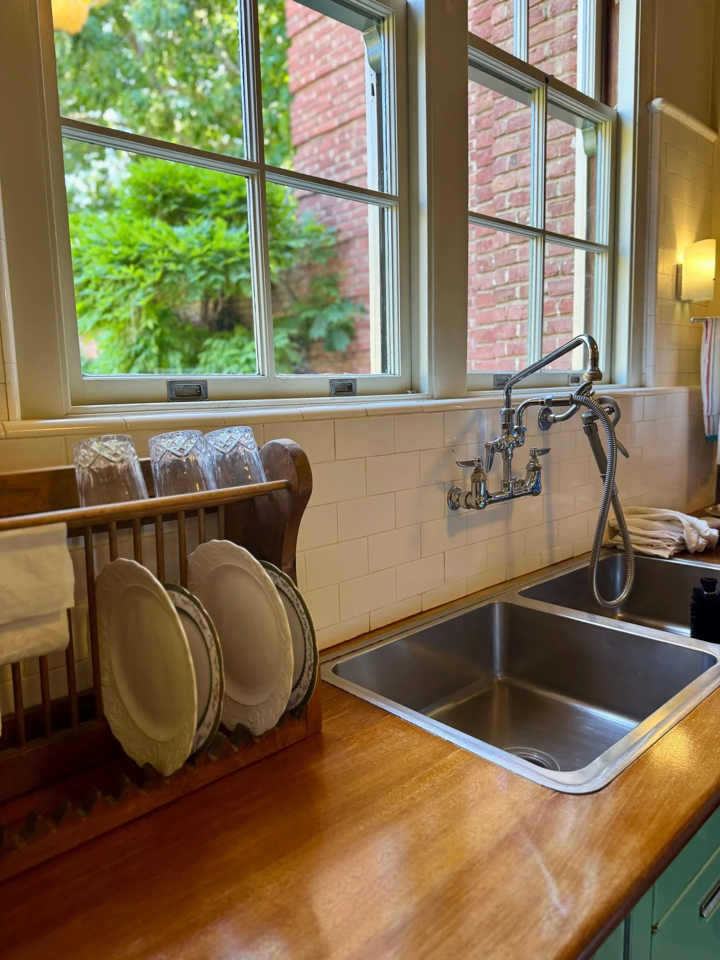 A kitchen sink beneath a window, with plates in a rack and wooden boards nearby.