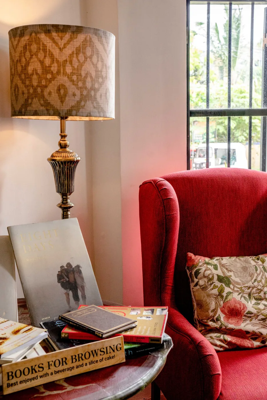 A red armchair beside a patterned lamp and a small stack of books.