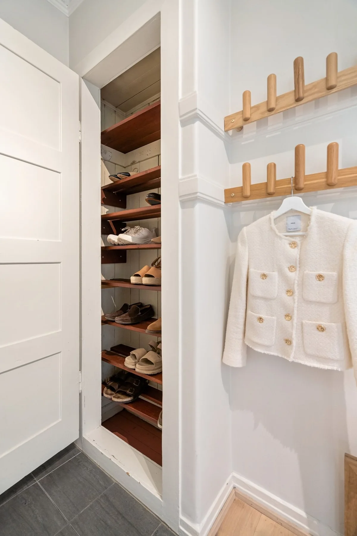 A shoe-storage cupboard beside wall hooks holding light jackets.