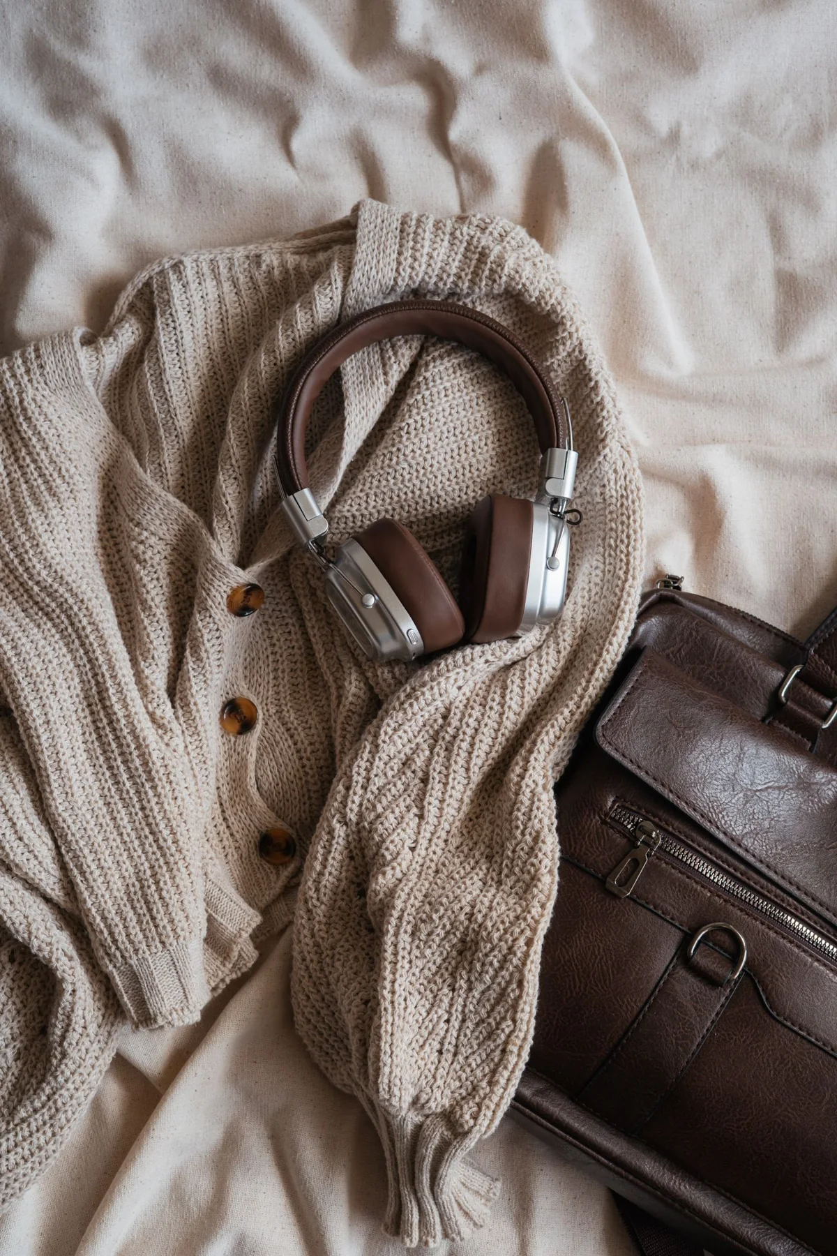 Knitwear, headphones and a brown bag arranged on a pale surface.
