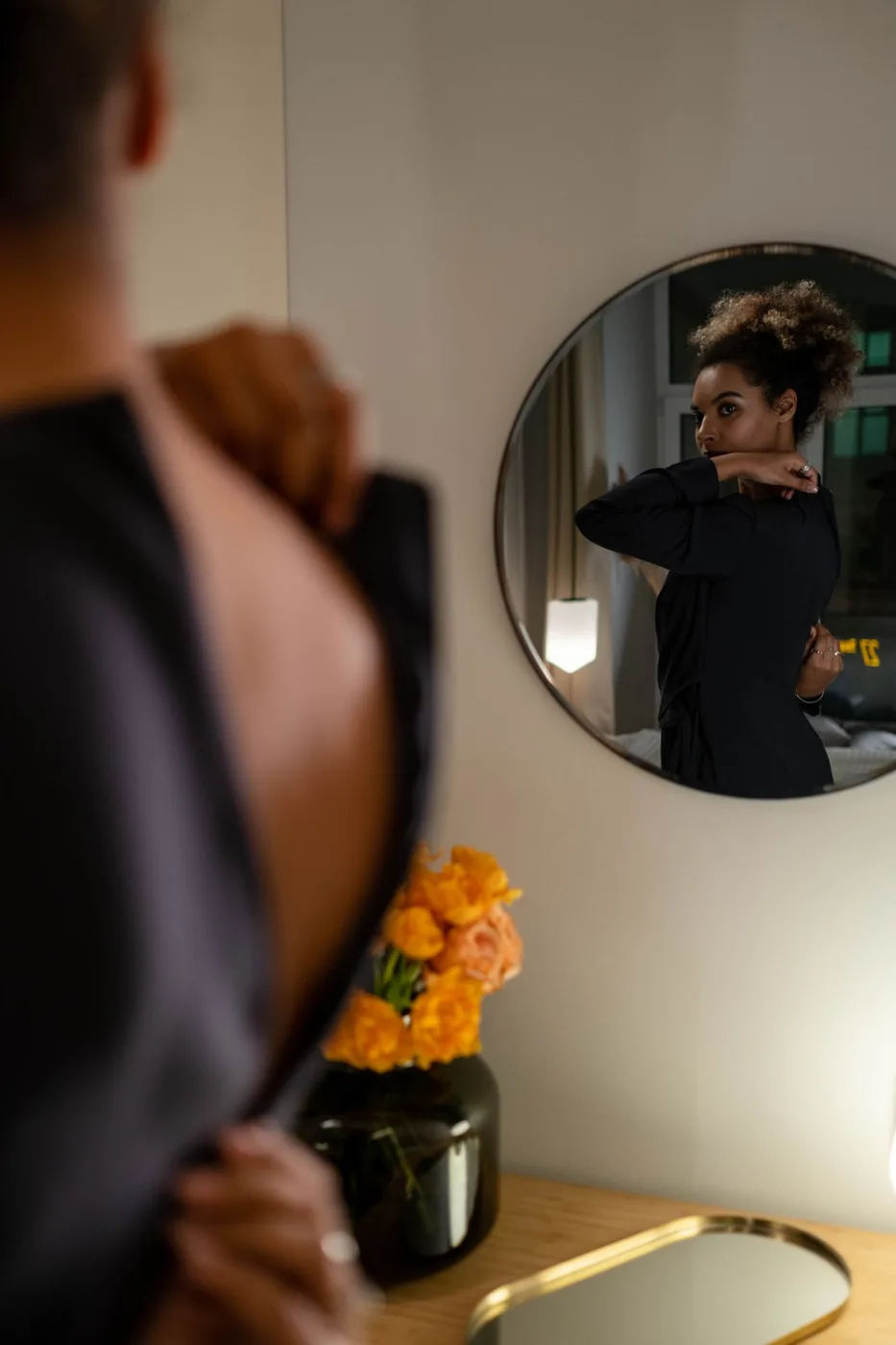 A person wearing a dark top seen in a round wall mirror.